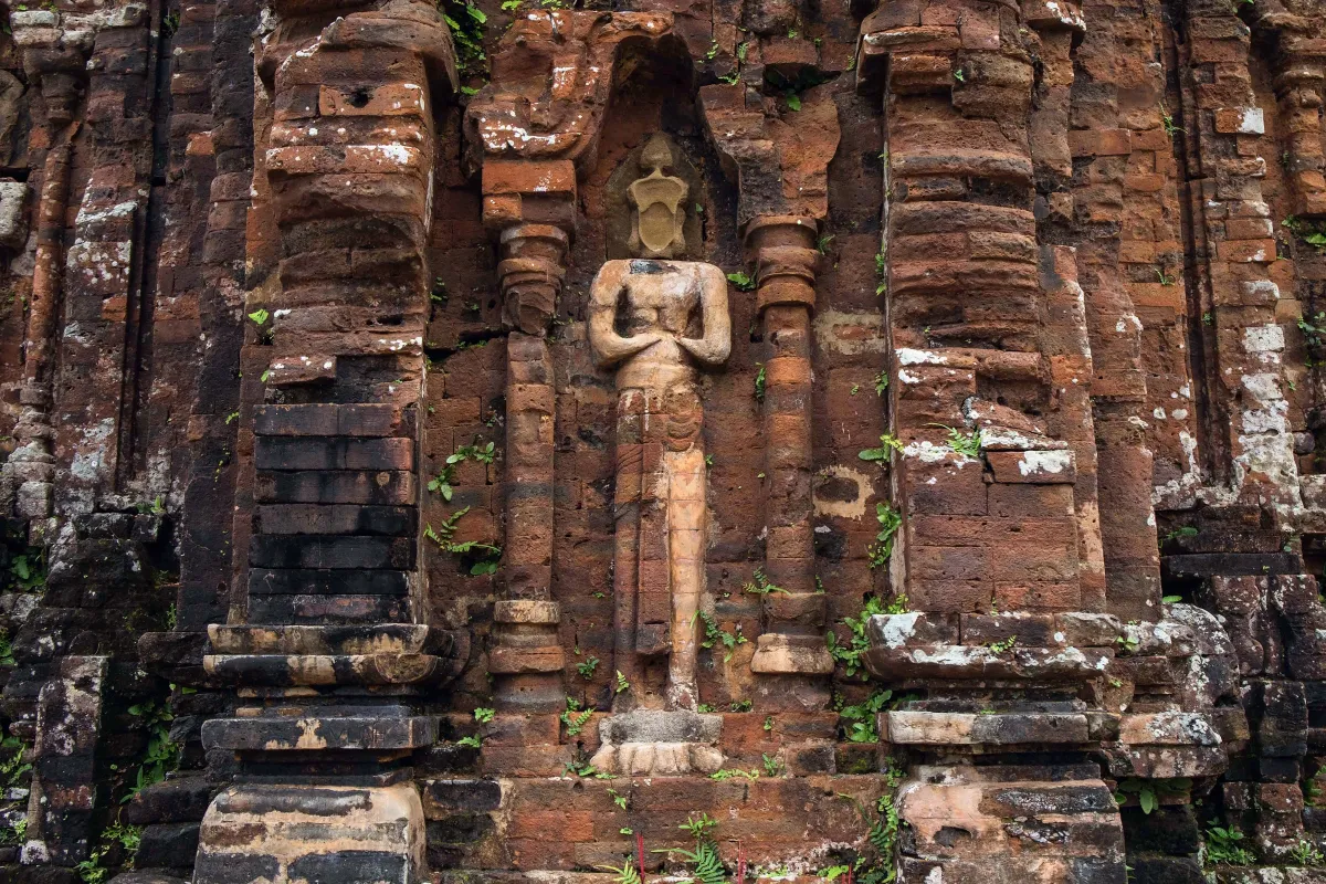 A carved standing figure in a niche on a moss-covered red-brick tower wall at My Son