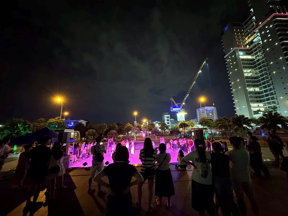 A crowd standing around a pink-lit open-air dance floor on Bach Dang walking street at night, with a tall building and a crane behind