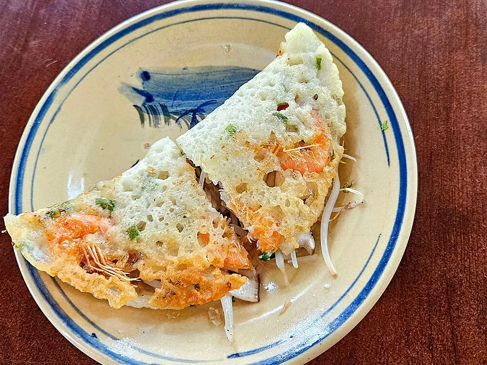 A folded bánh xèo with shrimp on a blue-and-white plate