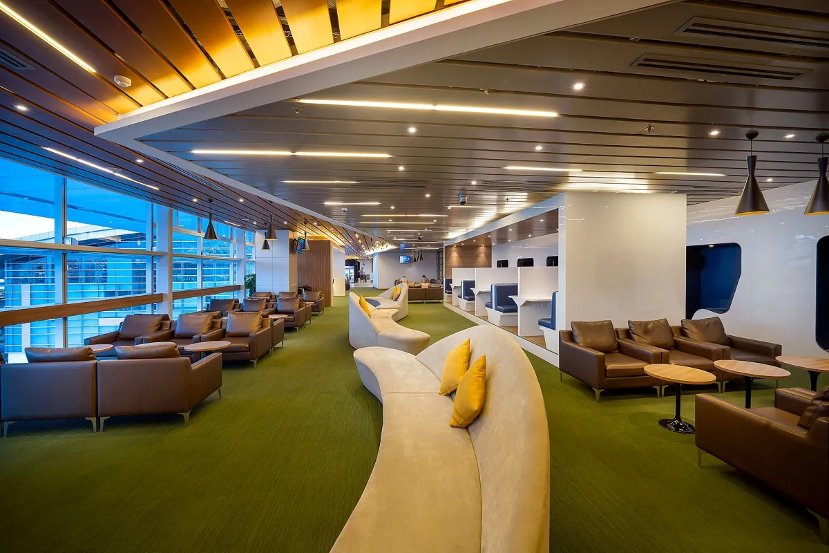A lounge in Da Nang's international terminal with brown leather armchairs, a curved cream sofa with yellow cushions and a large window