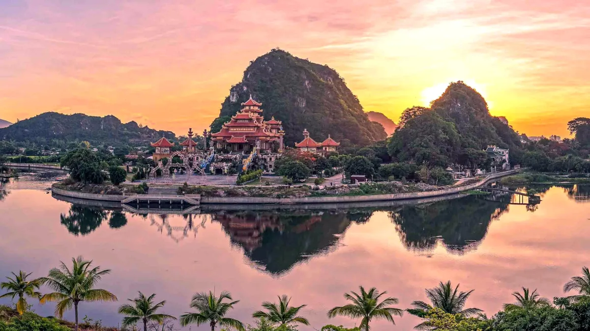 A pagoda at the foot of the Marble Mountains reflected in a lake at sunset