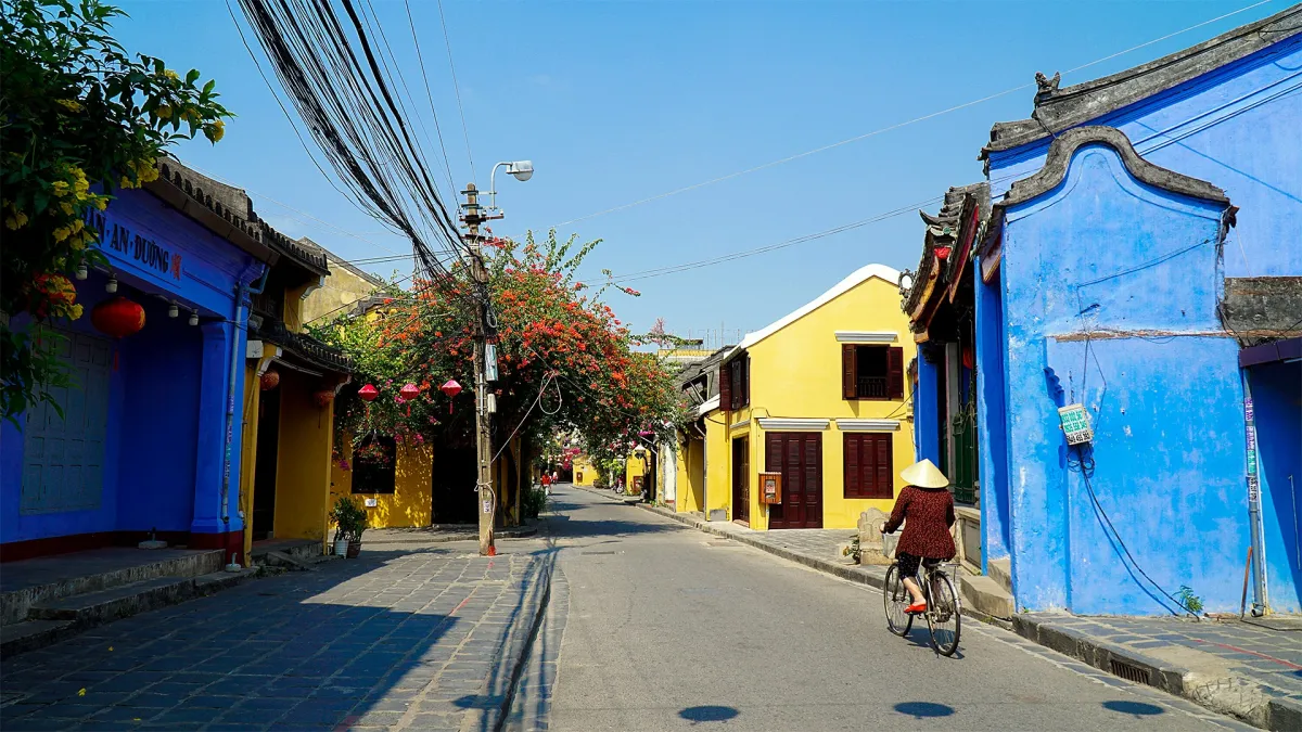 A quiet street of yellow and blue houses in Hoi An Ancient Town in the daytime, with one cyclist