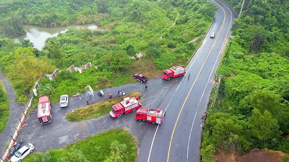 Aerial view of a winding mountain road through forest with fire engines and rescue vehicles parked beside it during an exercise
