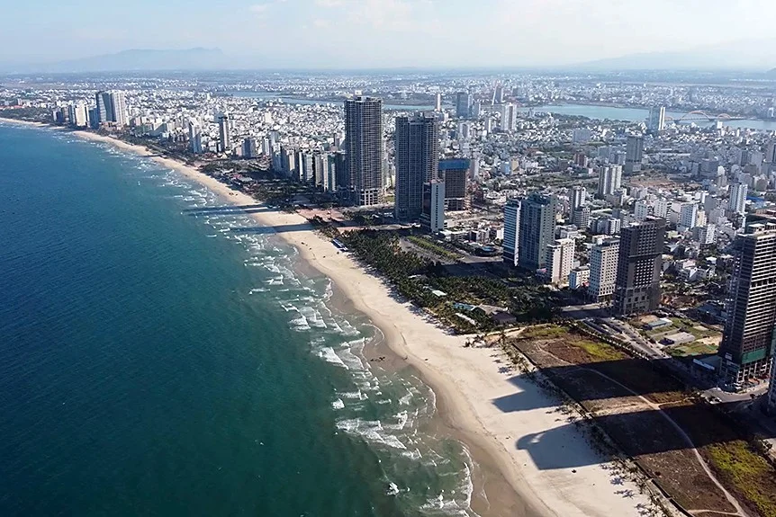 Aerial view of Da Nang's curving beachfront, with high-rise towers along the shore and the city stretching back to the Han River