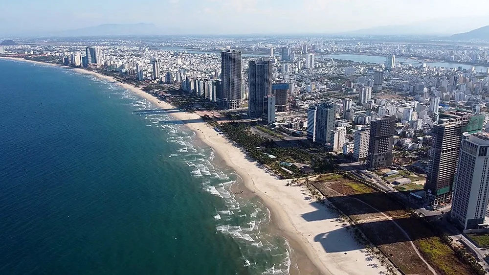 Aerial view of the Da Nang seafront, with a long curving beach, high-rise towers and the city stretching back to the Han River