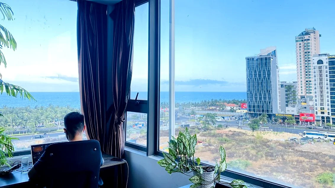 Corner desk by floor-to-ceiling windows on the ninth floor at Seaview Coworking, looking out over palm trees to the sea