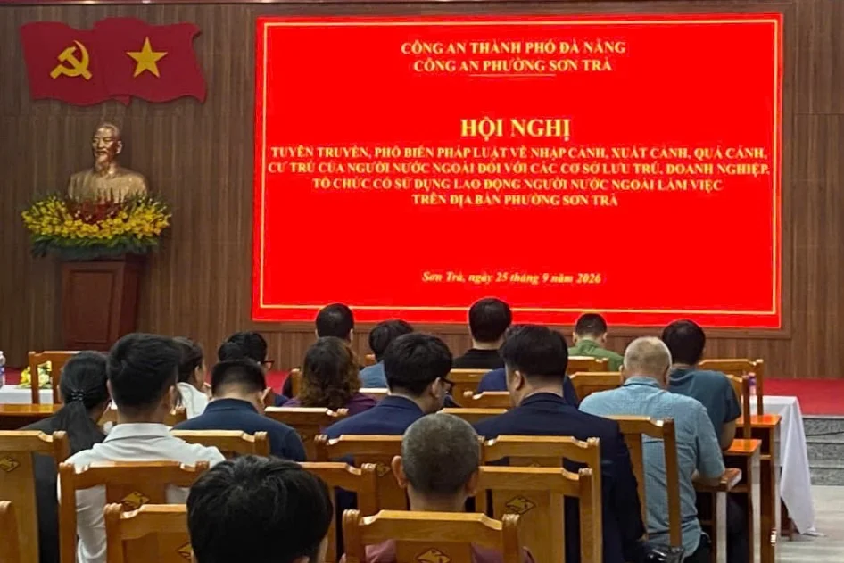 Delegates seen from behind at a ward police meeting in Son Tra, facing a red screen announcing a meeting on foreigners' entry, exit and residence