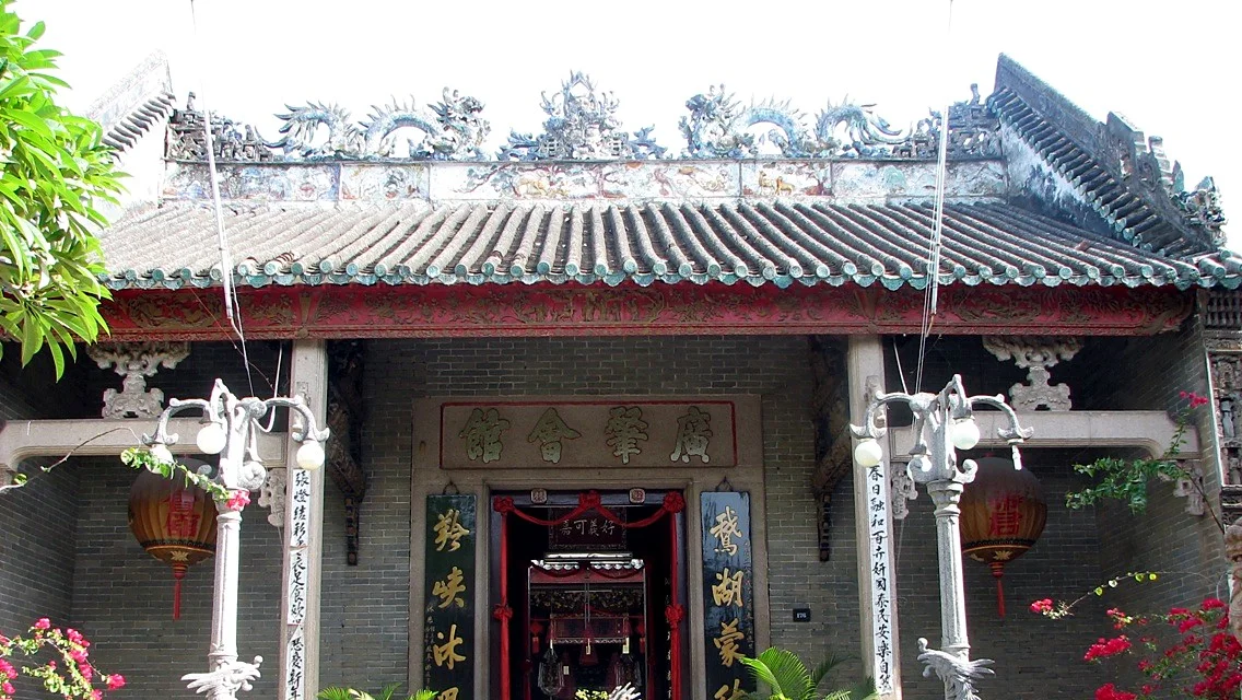 Front of the Cantonese Assembly Hall with a tiled roof, ceramic dragons along the ridge, a gold-lettered name board and two red lanterns