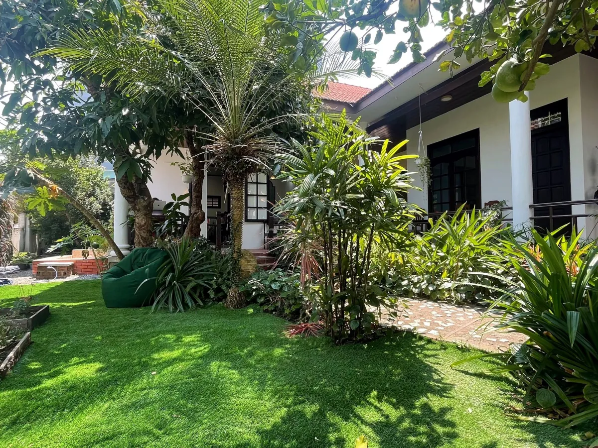 Garden with artificial grass, palms and a green beanbag in front of the white house with a tiled roof at Coworking Danang