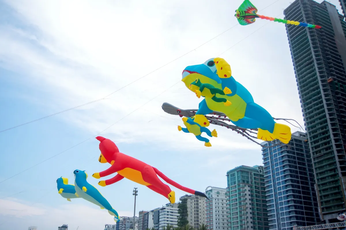 Giant animal-shaped kites flying between beachfront high-rise towers under a blue sky