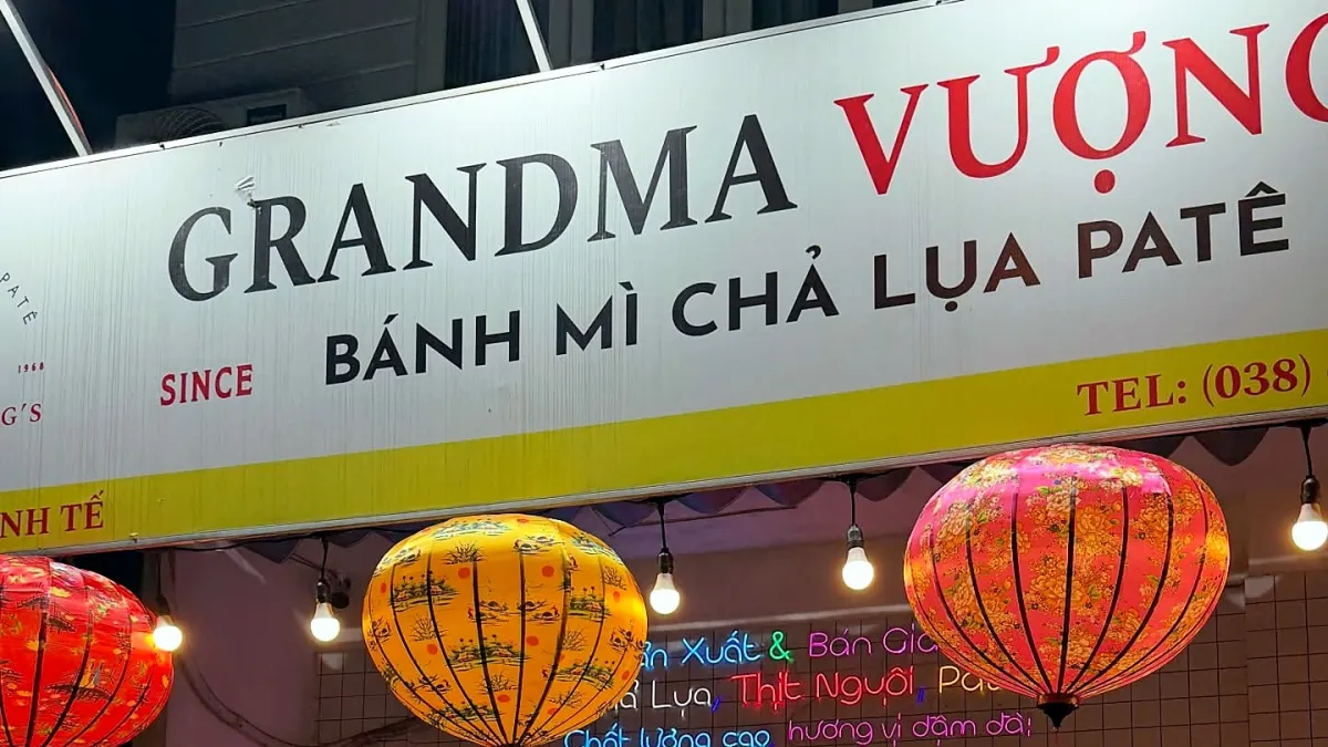 Grandma Vuong shop sign reading Banh mi cha lua pate above yellow, pink and red silk lanterns and neon lettering at night