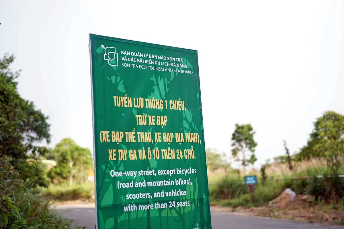 Green roadside sign in Vietnamese and English saying the road is one way and closed to bicycles, scooters and vehicles with more than 24 seats