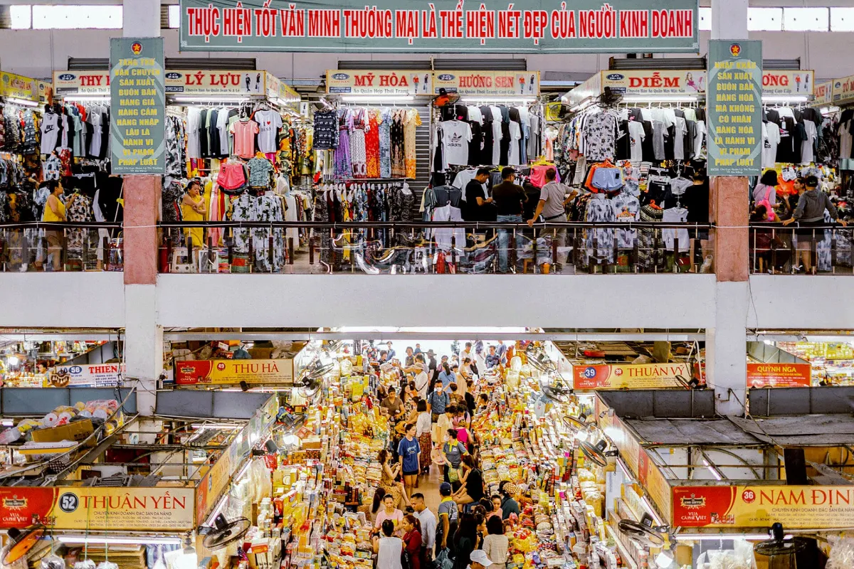 Inside Han Market seen from the upper floor: clothing stalls hung with shirts and dresses above, and a crowded aisle of dried food and specialty stalls below