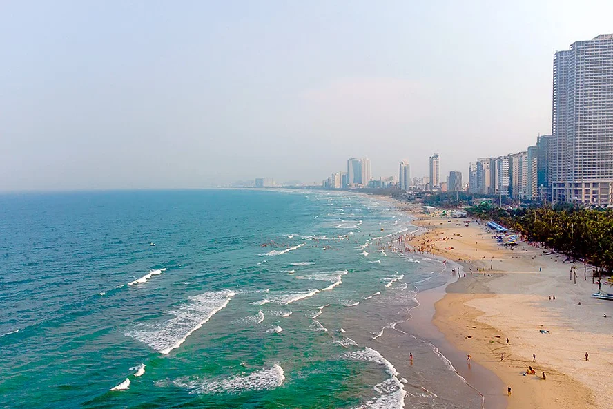 My Khe beach in Da Nang seen from the air, with waves breaking on a long stretch of sand and high-rise hotels along the shore