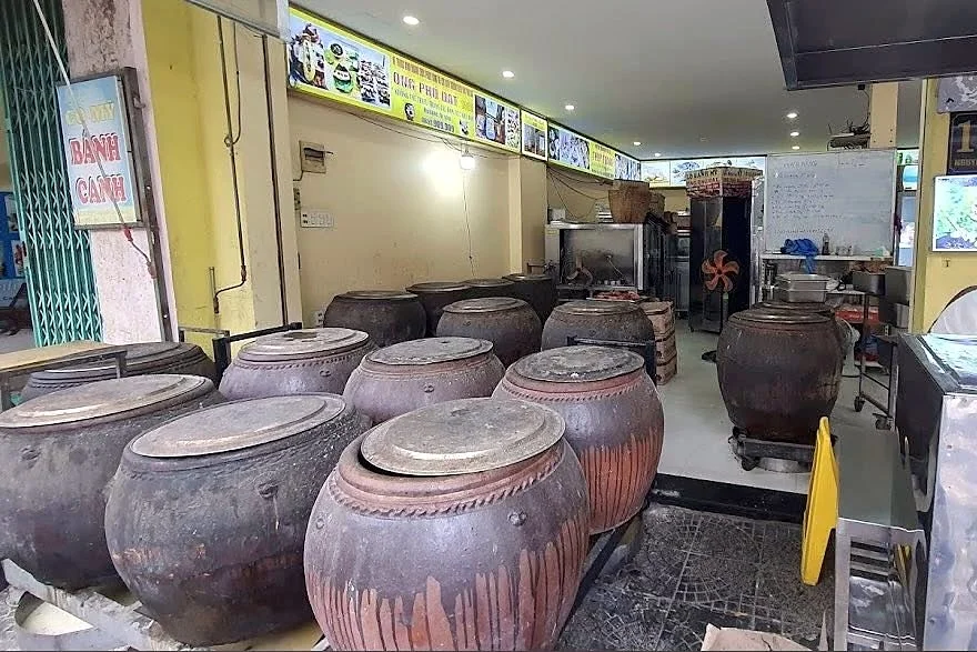 Rows of large lidded clay jars used for roasting pork at Heo Nuong Lu Ong Phu Dat, with a menu board above