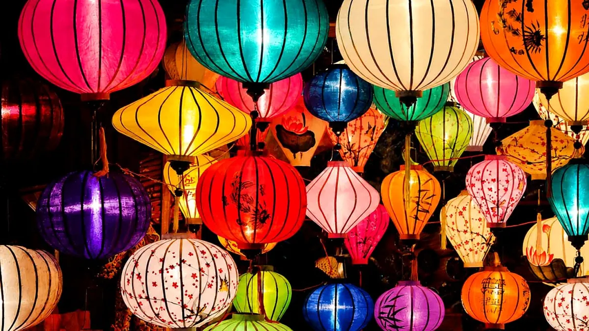Rows of lit silk lanterns in pink, teal, yellow, red and white hanging close together at night in Hoi An