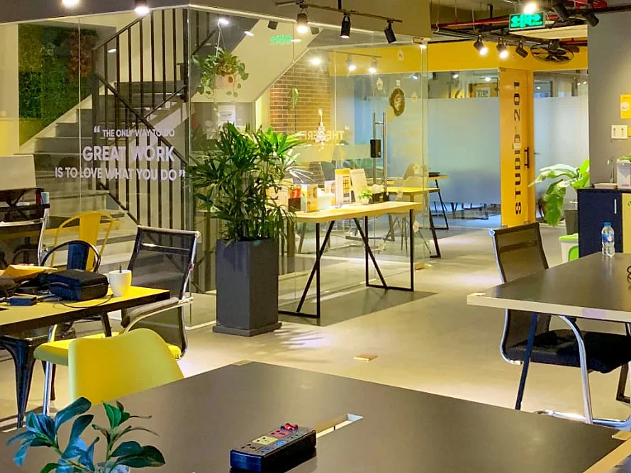 Shared work floor at Enosta Space with black desks, yellow chairs, a glass-walled staircase and a door marked Studio 201
