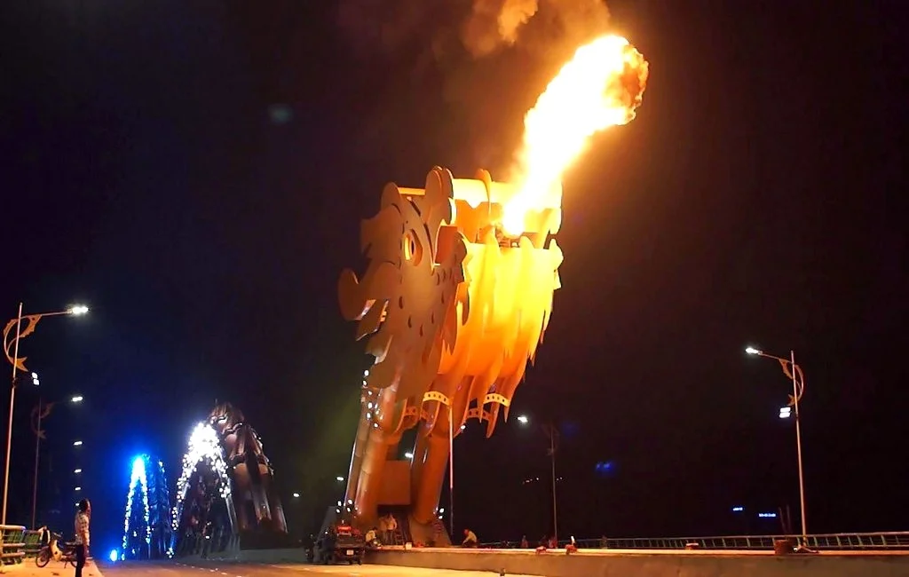 The dragon's head on the bridge at night, blowing a jet of orange fire into the dark sky