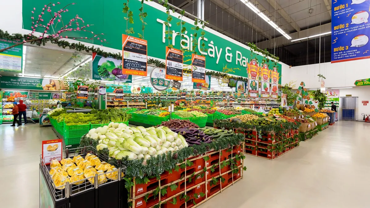 The fruit and vegetable section of a large supermarket, with wooden crates of cabbages, sweet potatoes and eggplants under a green sign reading Trái Cây & Rau, fruit and vegetables
