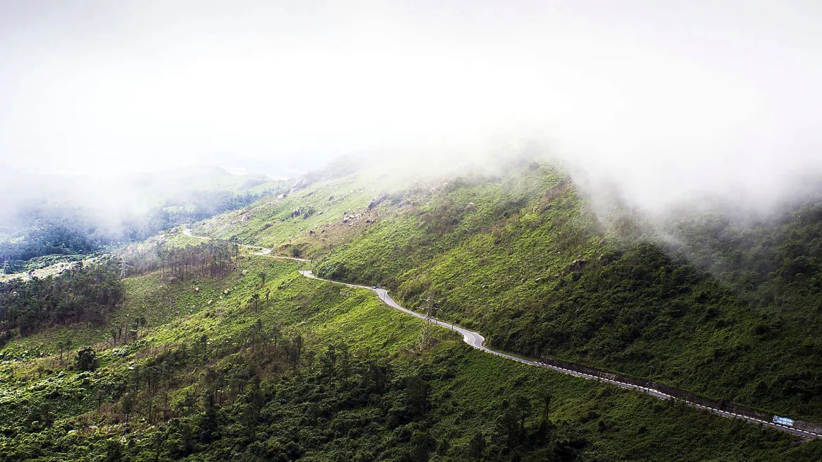 The Hai Van Pass road winding along a green mountainside under mist, seen from above